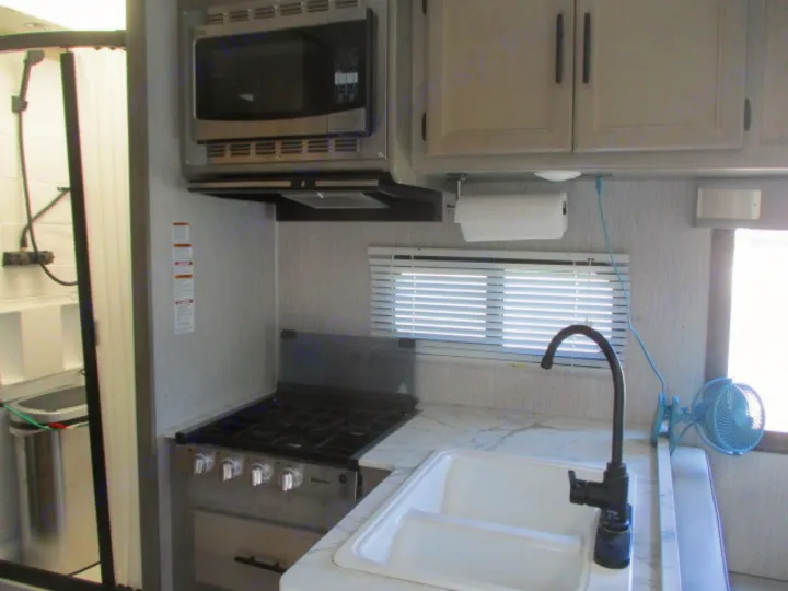 Modern RV rental interior showing a kitchen with microwave, stove, sink, and an adjacent shower stall. Bright and functional.. Coachmen Freelander 27QB 2021