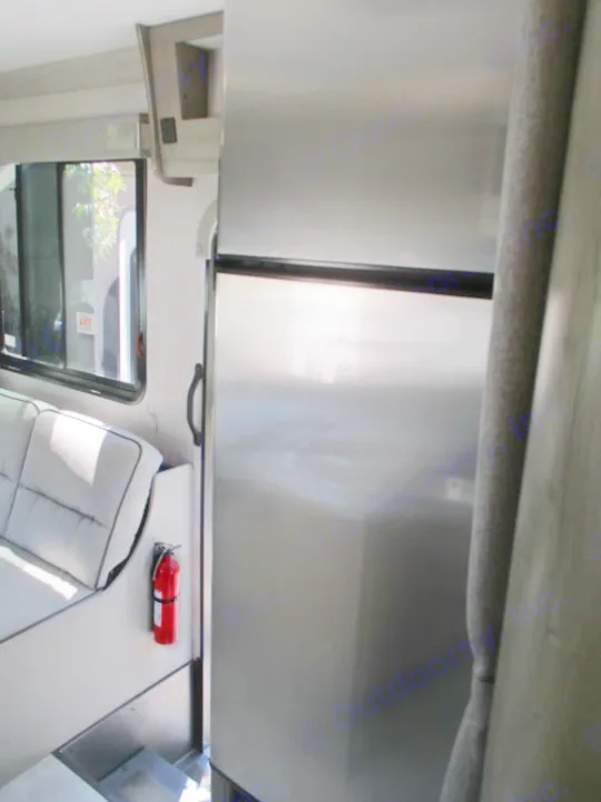 RV rental interior featuring a stainless steel fridge, comfortable dinette seating, and a mounted fire extinguisher.. Coachmen Freelander 27QB 2021