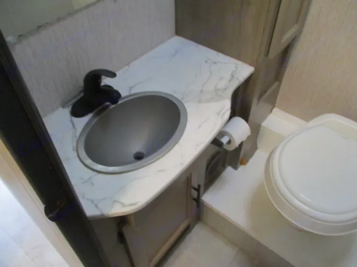 Inside an RV rental: a compact bathroom with a gray sink, black faucet, marble-look counter, and white toilet.. Coachmen Freelander 27QB 2021