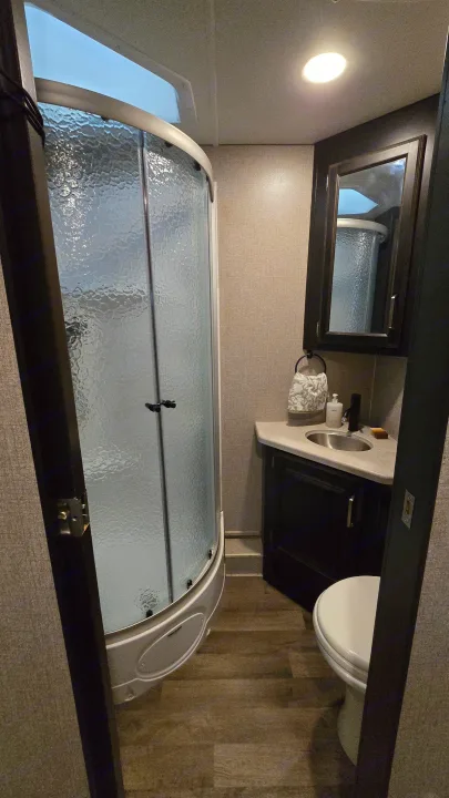 This RV rental's compact bathroom features a curved glass shower, modern vanity with sink, and a toilet.. Entegra Coach Vision XL 2021
