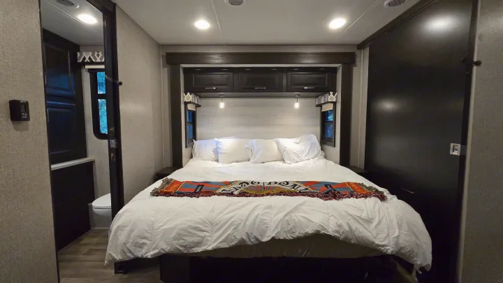 Bright & cozy **RV rental** bedroom. White bed, colorful throw, storage, & bathroom access. Ideal for comfortable travel.. Entegra Coach Vision XL 2021