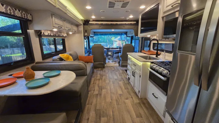 Bright RV rental interior showing a full kitchen, comfortable dinette seating, and panoramic windows. Ready for your next journey!. Entegra Coach Vision XL 2021