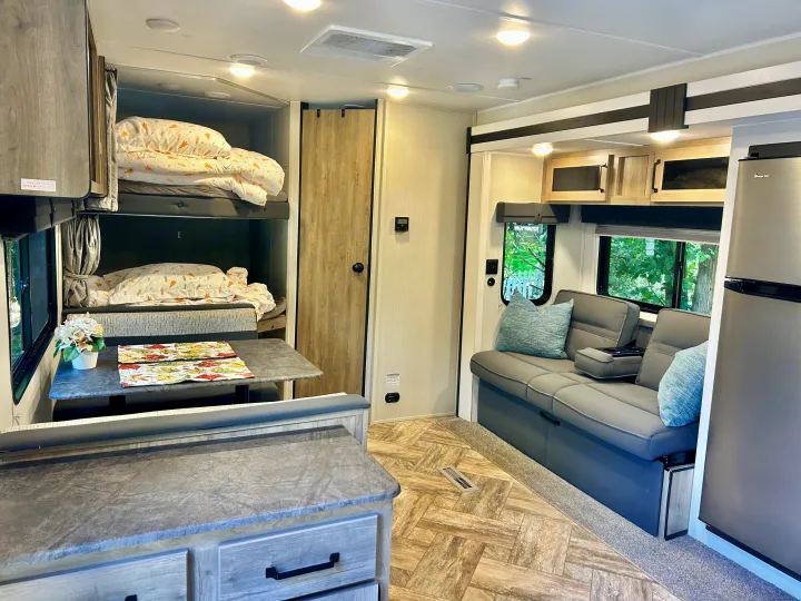 This rv rental features a cozy interior with bunk beds, a dinette, sofa, and a compact kitchen area, ideal for family travel.. Forest River Palomino Puma XLE 2023