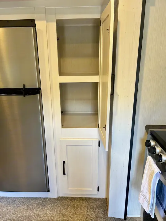 Inside an RV rental: a modern kitchen with a stainless steel fridge, open pantry, and stove.. Forest River Palomino Puma XLE 2023