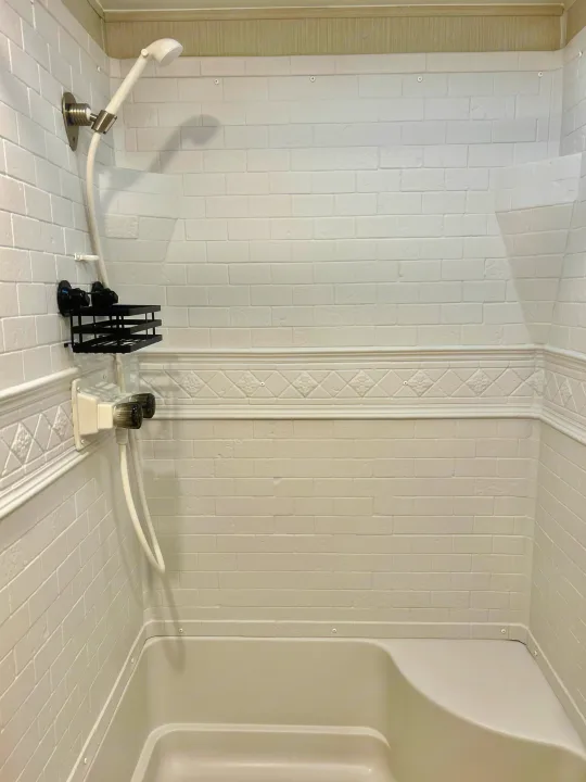 Compact and clean shower interior in an RV rental, featuring a handheld showerhead, small caddy, and light-colored tub.. Forest River Palomino Puma XLE 2023