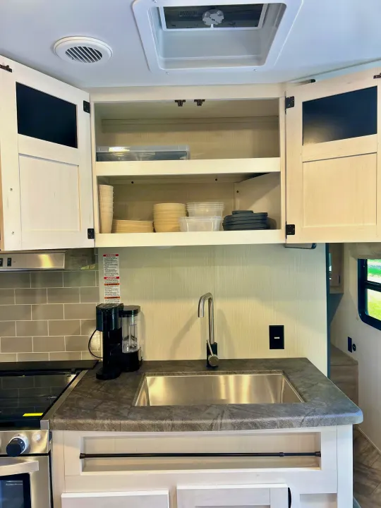 RV rental kitchen: light overhead cabinets, dark counters, sink, stove, and coffee maker in a compact setup.. Forest River Palomino Puma XLE 2023