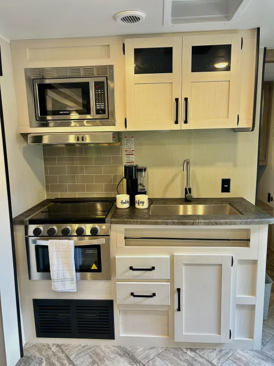 Modern RV rental kitchen featuring a stainless steel microwave, electric stove, sink, and light wood cabinets.. Forest River Palomino Puma XLE 2023
