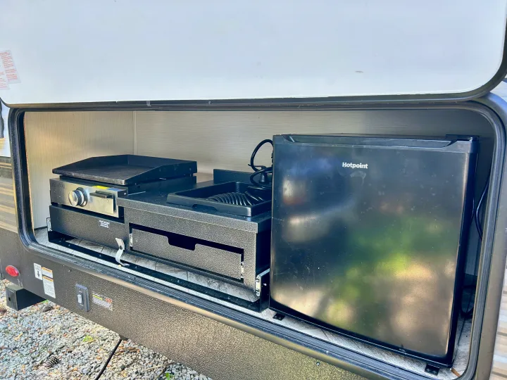 RV rental outdoor kitchen reveals a griddle, Hotpoint mini-fridge, and a pull-out sink/hose system.. Forest River Palomino Puma XLE 2023