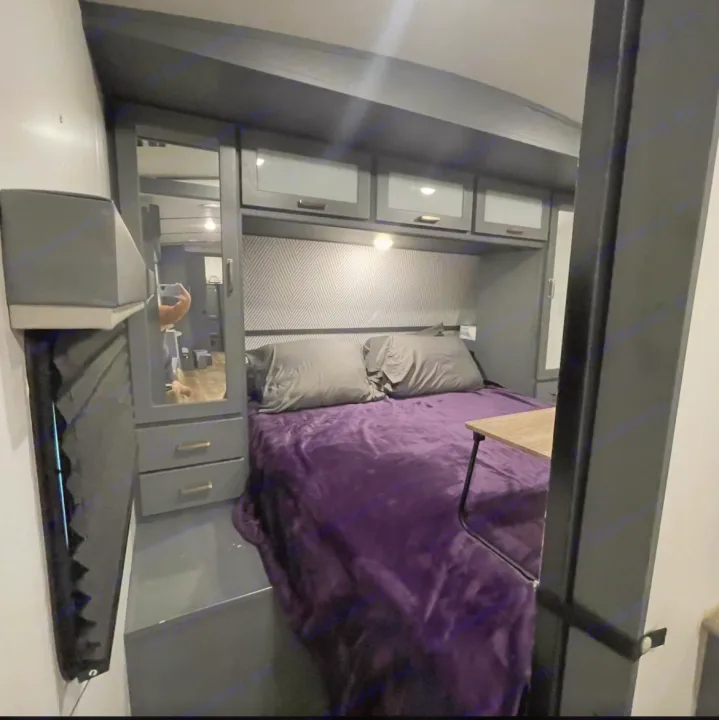 Cozy RV rental bedroom featuring a purple bed, gray pillows, mirrored closet, and overhead storage.. Keystone RV Bullet Ultra Lite 2022