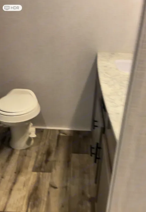 This RV rental bathroom features a compact white toilet, a marble-patterned counter with a sink, and wood-look flooring.. Dutchmen Coleman Light 2022