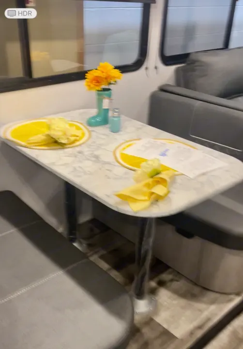 Visually, an RV rental's bright dining area: marble table with yellow lemon decor, flowers, and plush benches.. Dutchmen Coleman Light 2022