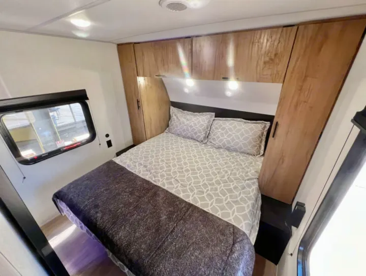 RV rental: A cozy bedroom with a large bed, wood-grain overhead cabinets, and a side window, providing comfortable travel.. Forest River Cherokee Grey Wolf 2026