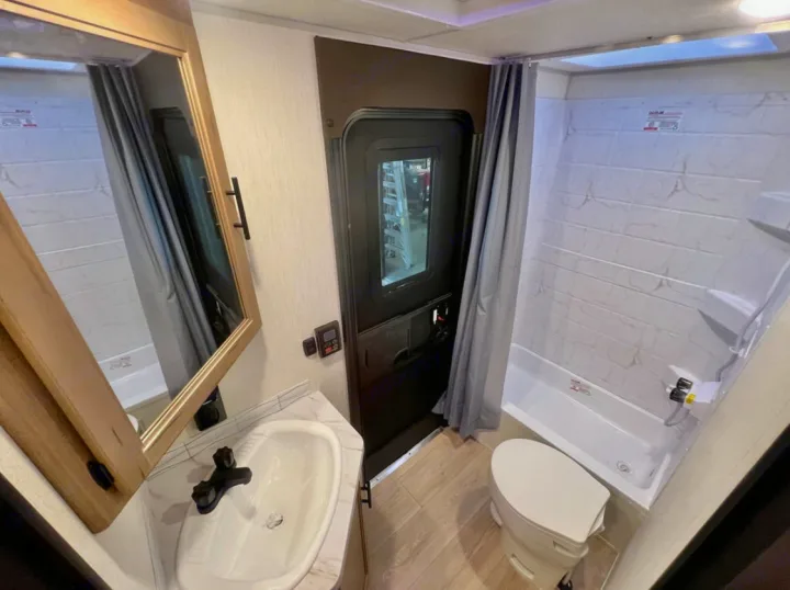 Explore this compact RV rental bathroom: a white sink, modern black faucet, vanity mirror, toilet, and shower with curtain.. Forest River Cherokee Grey Wolf 2026