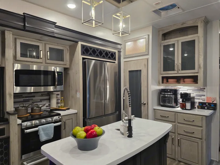This modern RV rental kitchen features stainless steel appliances, light cabinetry, a central island, and stylish lighting.. Keystone RV Alpine Avalanche 2024