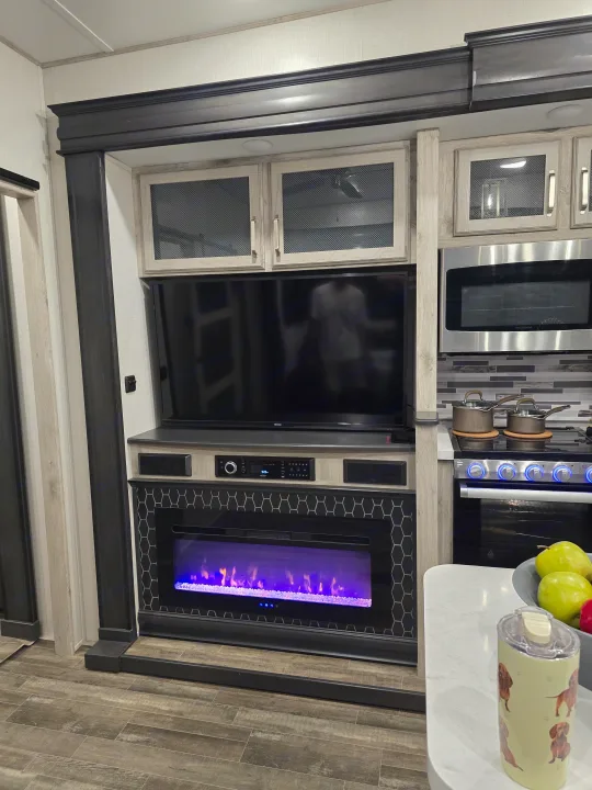 Modern RV rental interior with an entertainment center, electric fireplace, and kitchen area.. Keystone RV Alpine Avalanche 2024