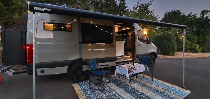 Cozy RV rental evening: Sprinter camper van with awning, string lights, and outdoor dining area set up.. Activan Cypress 170 2022