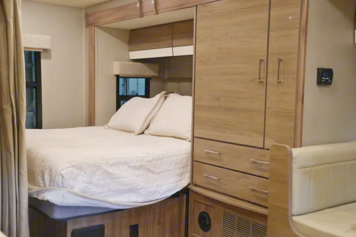 Cozy bedroom and storage in an RV rental, featuring a comfortable bed, overhead cabinets, and built-in wardrobe.. Entegra Coach Qwest 2019