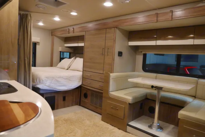 This RV rental interior features a bright living space with a comfortable bed, wood cabinetry, and a dinette.. Entegra Coach Qwest 2019