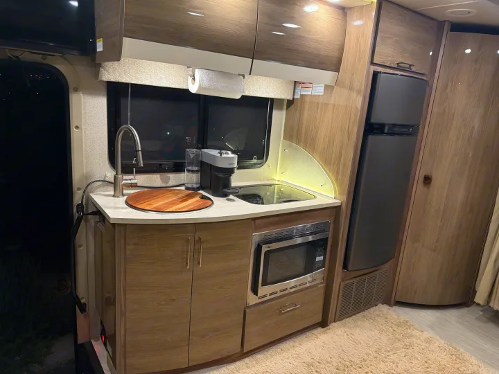 Sleek RV rental kitchen with modern appliances: sink, coffee maker, stovetop, microwave, and fridge.. Entegra Coach Qwest 2019