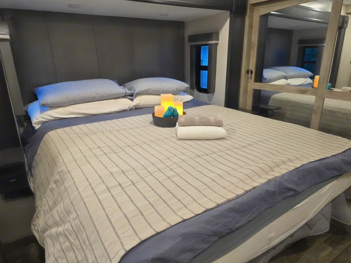 This RV rental offers a comfy bedroom with striped bedding, glowing candles, and plush towels for your relaxation.. Keystone RV Alpine Avalanche 2024