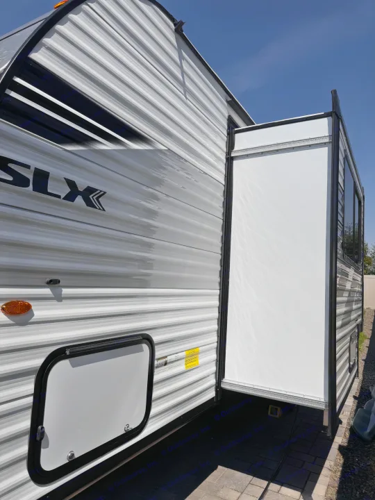 Side view of a modern gray and white corrugated RV rental with an extended white slide-out room, parked on pavers under a clear blue sky.. Jayco Jay Flight 2026