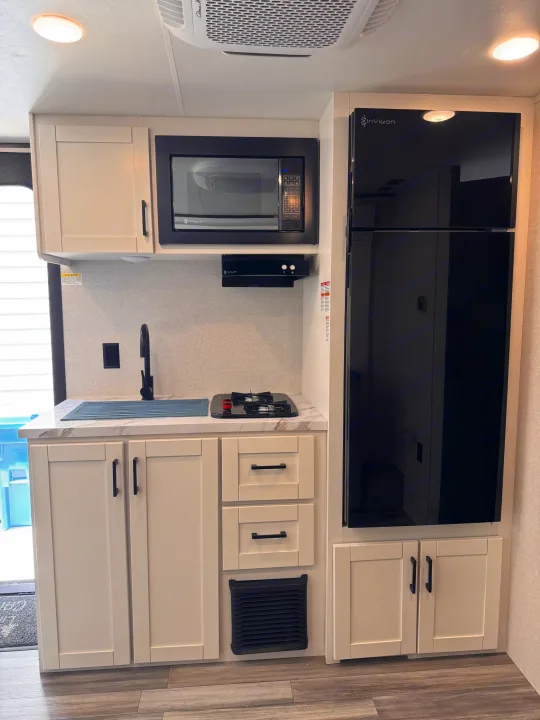 Modern RV rental kitchen with white cabinets, black appliances (microwave, fridge, stove), sink, and wood-look floor.. Jayco Jay Flight 2026