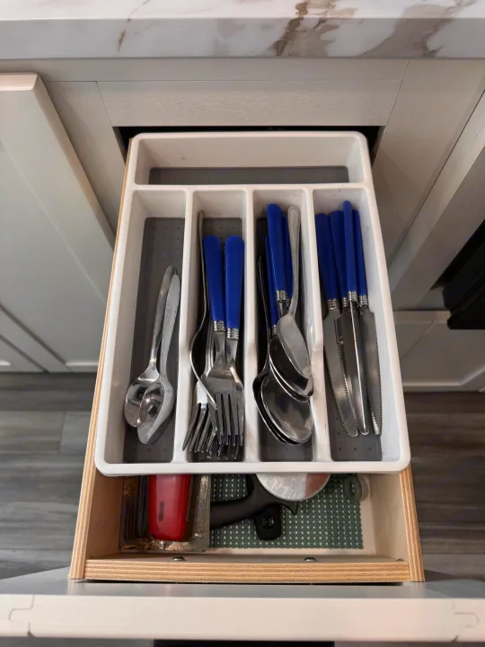 Organized RV rental kitchen drawer: white utensil tray with blue-handled forks, knives, spoons, plus a pizza cutter.. Jayco Jay Flight 2026