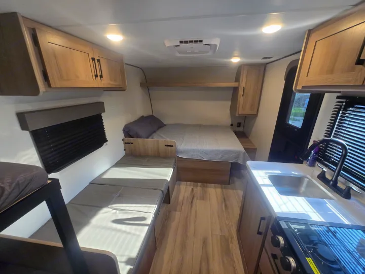 Clean RV rental interior featuring a bedroom area with a main bed and bunk beds, plus a compact kitchenette.. Keystone Colman 2025