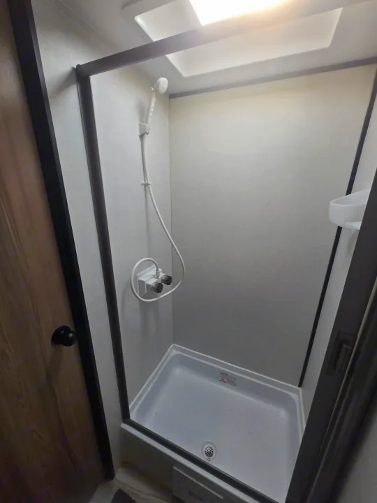Clean, compact shower stall in an RV rental, complete with handheld showerhead and overhead skylight.. Keystone Colman 2025