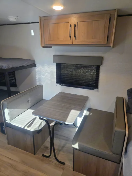 Compact RV rental interior featuring a practical dinette, bunk beds, and overhead storage cabinets.. Keystone Colman 2025