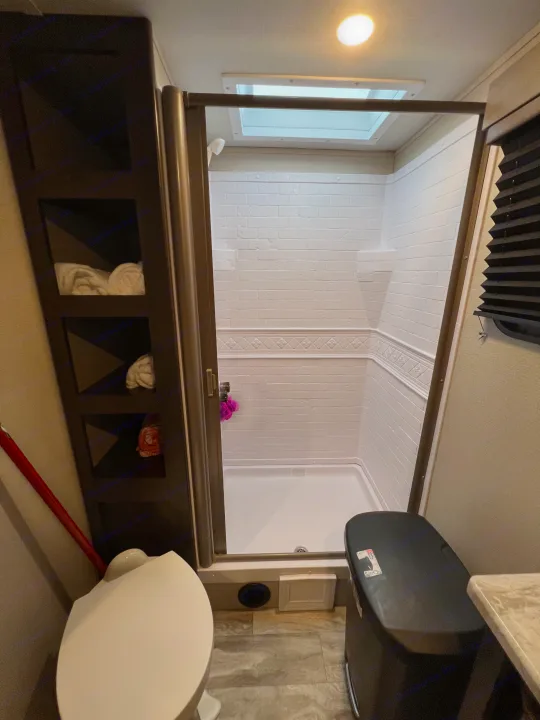 Compact RV rental bathroom with a functional shower, toilet, and built-in storage shelves. Ideal for travel.. Grand Design Transcend Xplor 2022