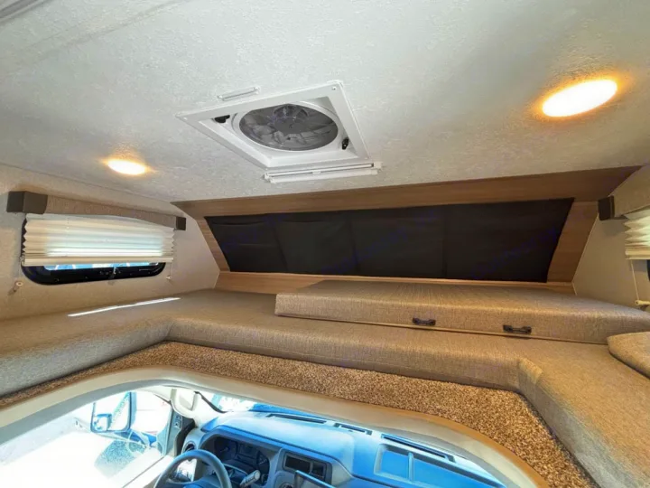Spacious RV rental overhead bunk and sleeping area, featuring a window, ceiling fan, and cozy interior lighting.. Adventurer 19RK113 2014