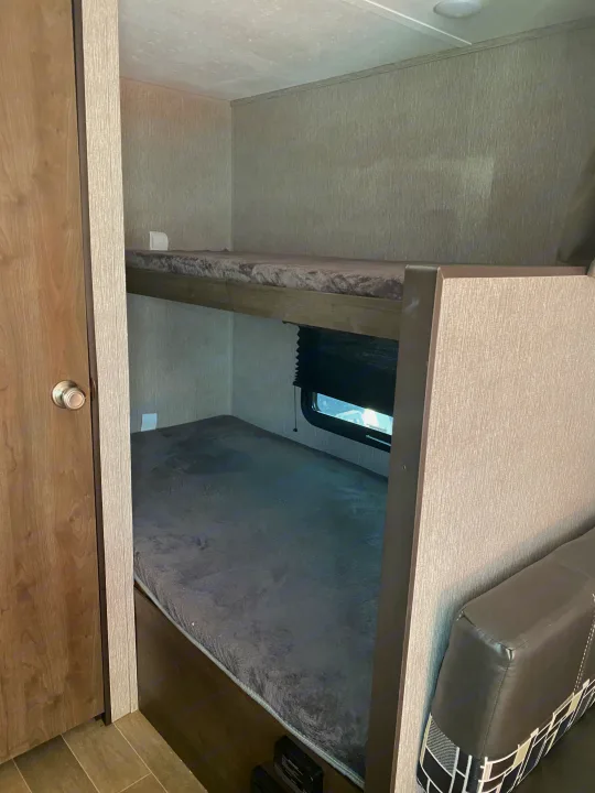 This RV rental features stacked bunk beds with soft gray mattresses, a window on the lower bunk, and a cozy sleeping area.. Dutchmen Coleman Lantern LT 2020