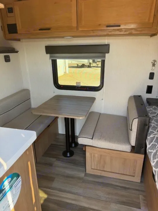View of a compact rv rental interior: dinette with table & bench seating, overhead cabinets, and an adjacent bed.. Cherokee WOLF PUP  16BHSBL 2023