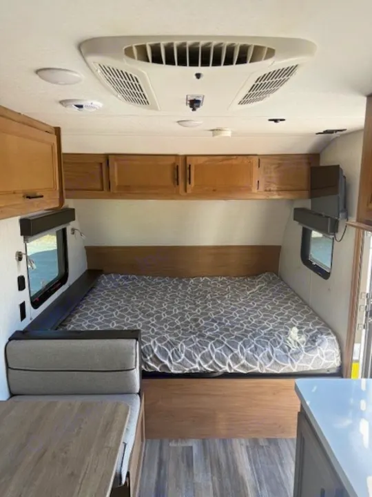 Interior of an RV rental showing a bed, dinette, overhead cabinets, TV, AC unit, and small kitchenette area.. Cherokee WOLF PUP  16BHSBL 2023