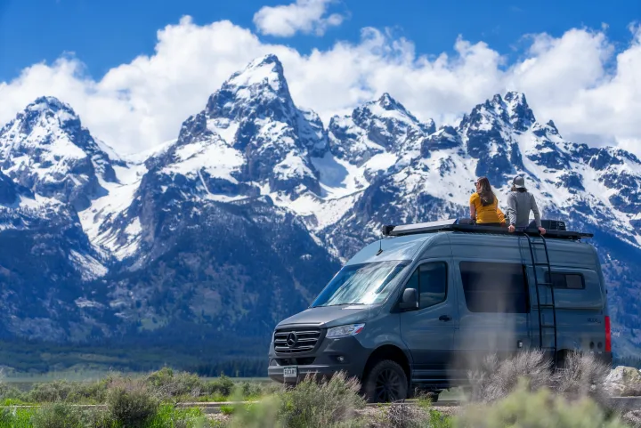 Couple on an RV rental enjoys majestic snow-capped mountains from their camper van roof.. Storyteller Overland Storyteller Overland Class B 2021