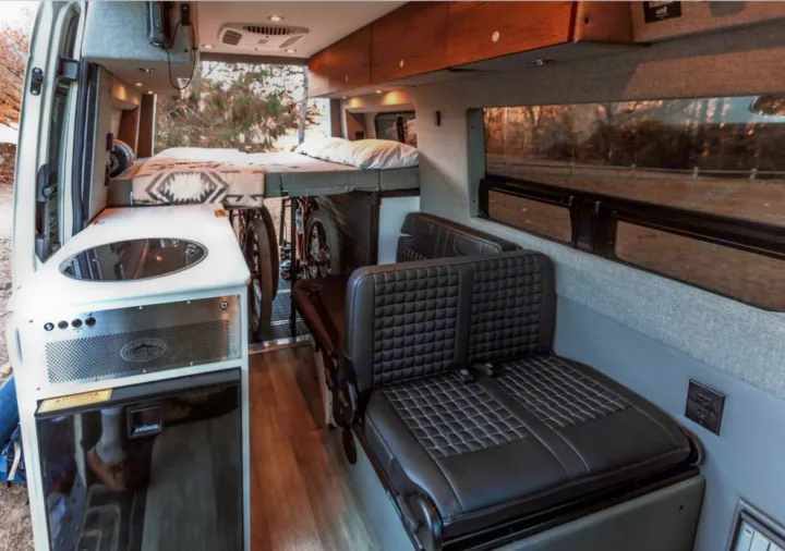 Interior of a modern rv rental camper van, featuring a bed, kitchen, seating area, and clever bike storage.. Storyteller Overland Storyteller Overland Class B 2021