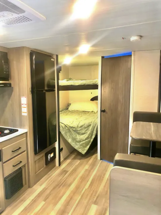 This RV rental's interior features a kitchen, bunk beds, and dinette, all on light wood-look flooring. Ready for travel!. Keystone RV Hideout Sport 2024