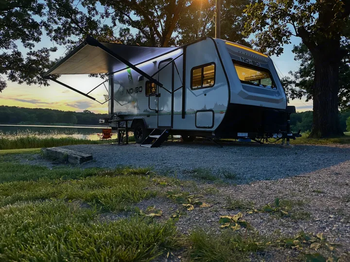 Modern RV rental at dusk, parked lakeside with illuminated awning for a cozy evening campsite.. No Boundaries 19 2021