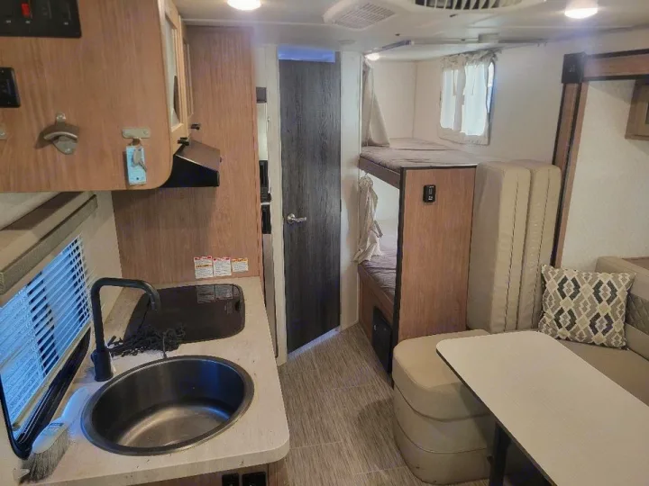 This RV rental's interior features a compact kitchen with sink, bunk beds, and dinette seating, ready for travel.. No Boundaries 19 2021