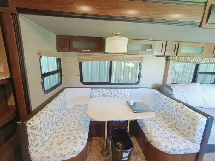 RV rental interior with a cozy dinette featuring floral U-shaped bench seating, table, and overhead storage cabinets.. Dutchmen Aerolite 28dbhs 2017