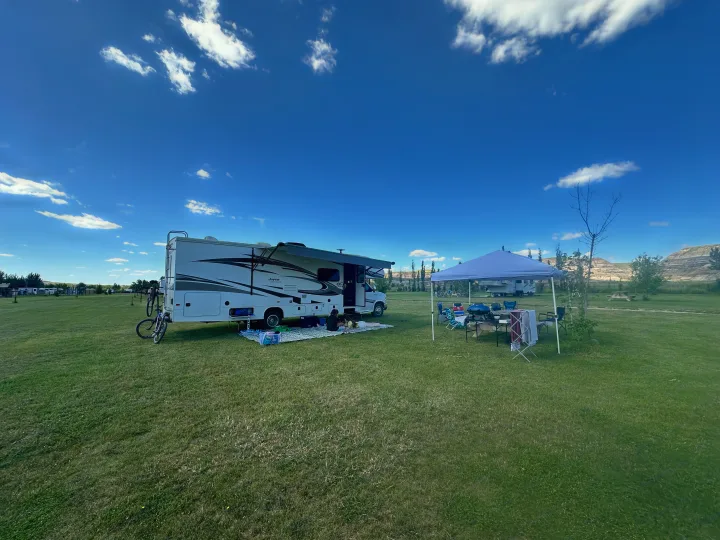 RV rental adventure: A white RV is set up with an extended awning, bicycles, and a pop-up canopy on a grassy campsite.. Jayco Greyhawk 2019