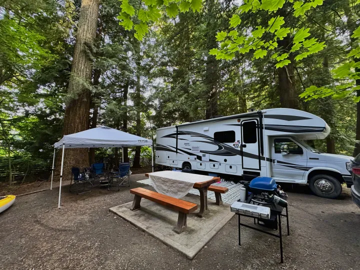 A spacious RV rental is parked at a tranquil campsite, complete with a canopy, picnic table, and grill for outdoor living.. Jayco Greyhawk 2019