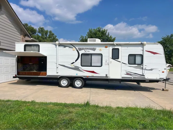 Spacious white travel trailer RV rental with a convenient outdoor kitchen setup, parked on a concrete driveway.. Forest River Wildwood X-Lite 2013
