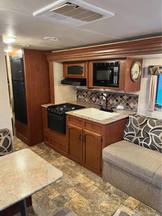 Step into this RV rental, featuring a compact kitchen with a stove, microwave, sink, and a comfortable dining area.. Forest River Wildwood X-Lite 2013