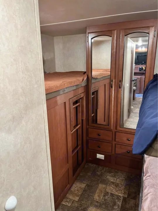 Compact RV rental bunk beds with integrated storage and mirrored doors, showcasing efficient interior design.. Forest River Wildwood X-Lite 2013