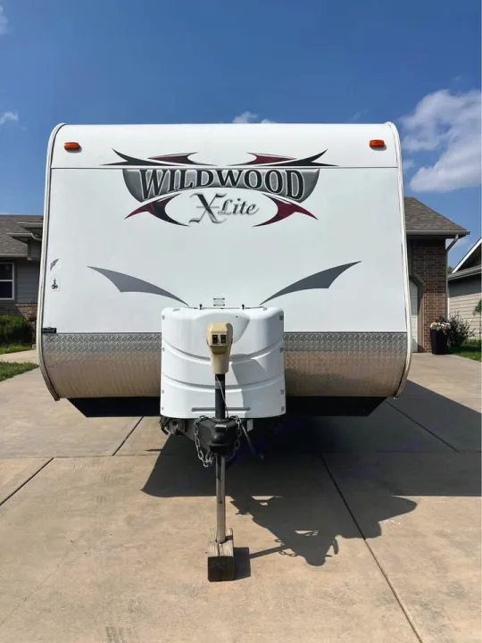 White Wildwood X-Lite travel trailer parked on a driveway under a blue sky, ready for your RV rental adventure.. Forest River Wildwood X-Lite 2013