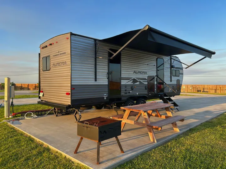 Sunny RV rental site with travel trailer, extended awning, picnic table, and grill. Perfect for outdoor living.. Forest River 26FKDS 2025