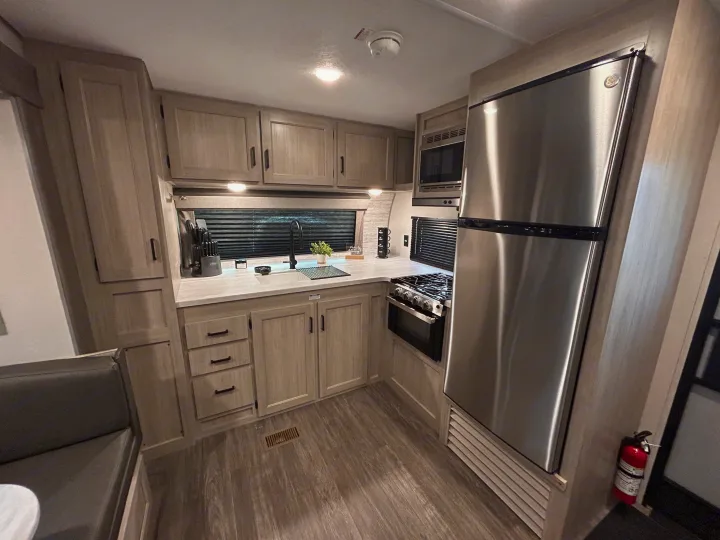 Modern RV rental kitchen. Features stainless fridge, oven, microwave, sink, light wood cabinets & seating. Bright, clean space.. Forest River 26FKDS 2025
