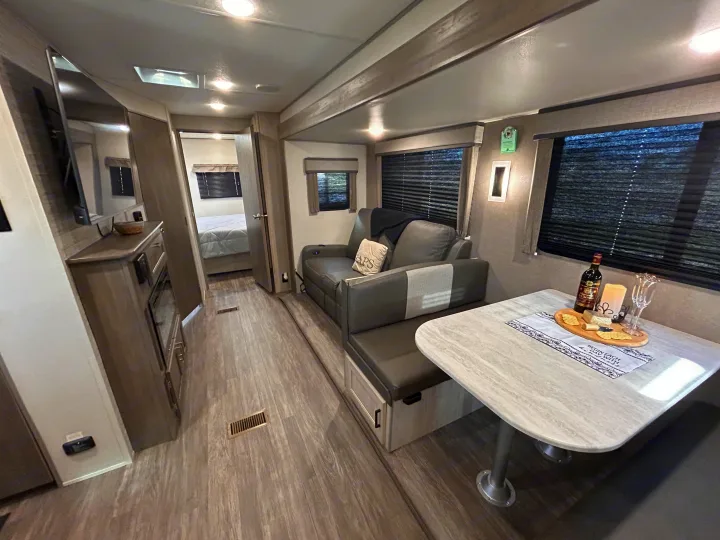 Modern RV rental interior showing a comfortable living area, dinette with snacks, and a peek into the bedroom.. Forest River 26FKDS 2025